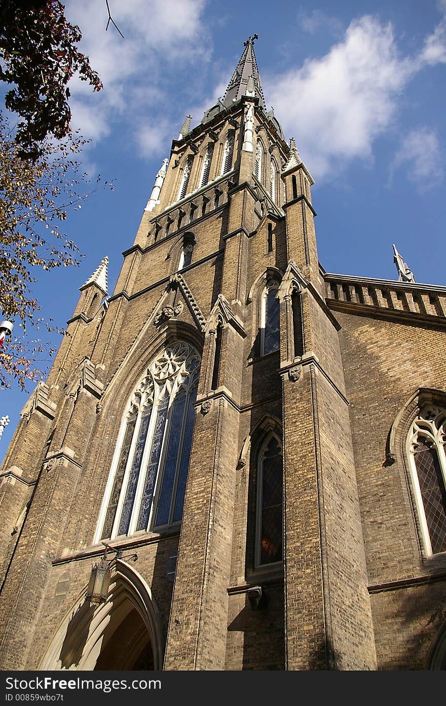 An upward view of a gothic architecture church with a spire (steeple) against a blue sky background. An upward view of a gothic architecture church with a spire (steeple) against a blue sky background