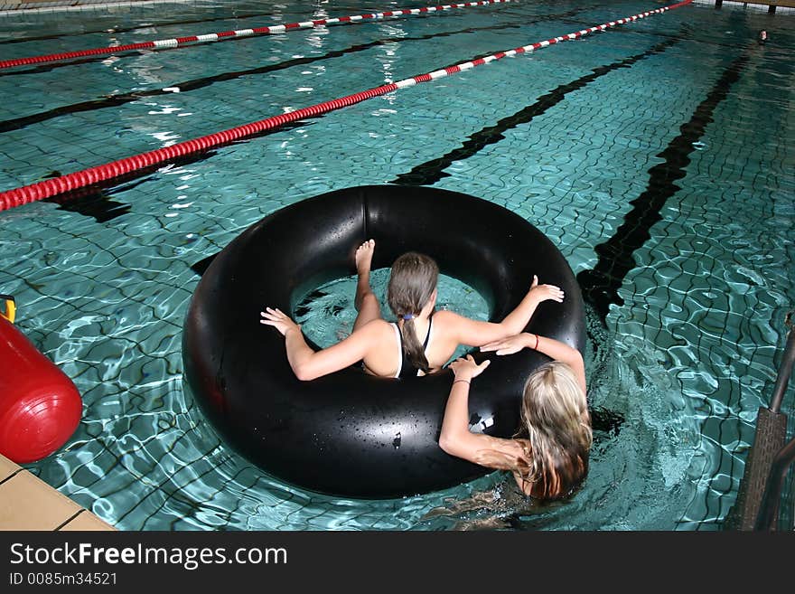 Indoor swimming pool fun, two girls playing with a big black buoy