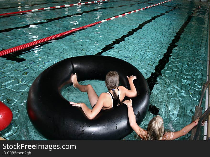 Indoor swimming pool fun, two girls playing with a big black buoy