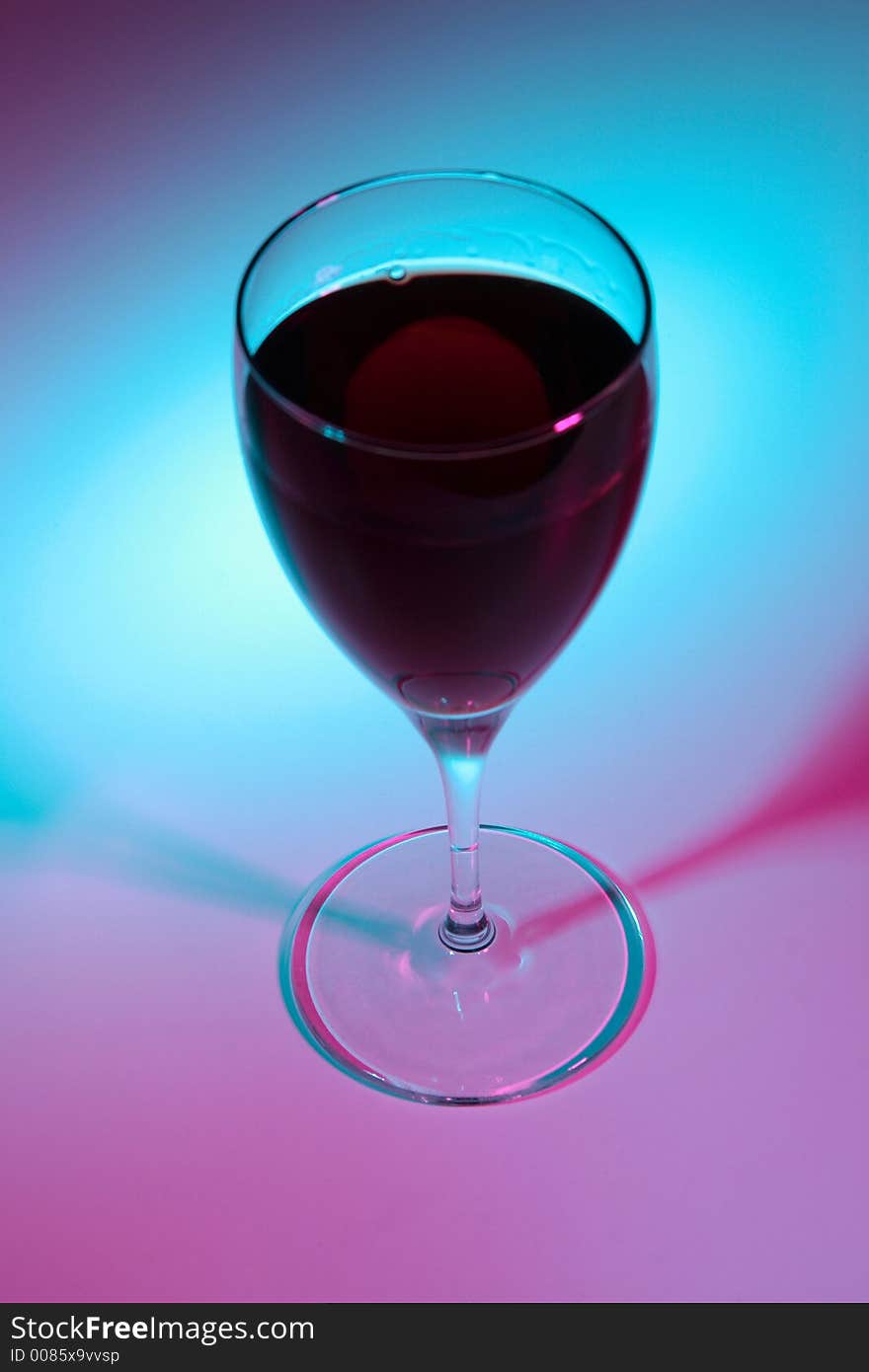 Glass of red wine lit by colour lights, focused on bottom.