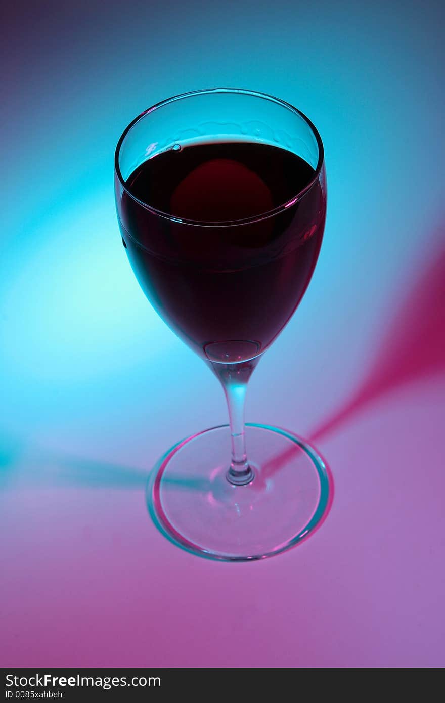 Glass of red wine lit by colour lights, focused on top.