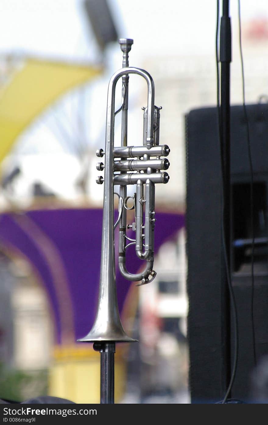 A silver trumpet sitting on a stand on stage at an outdoor jazz festival. A silver trumpet sitting on a stand on stage at an outdoor jazz festival