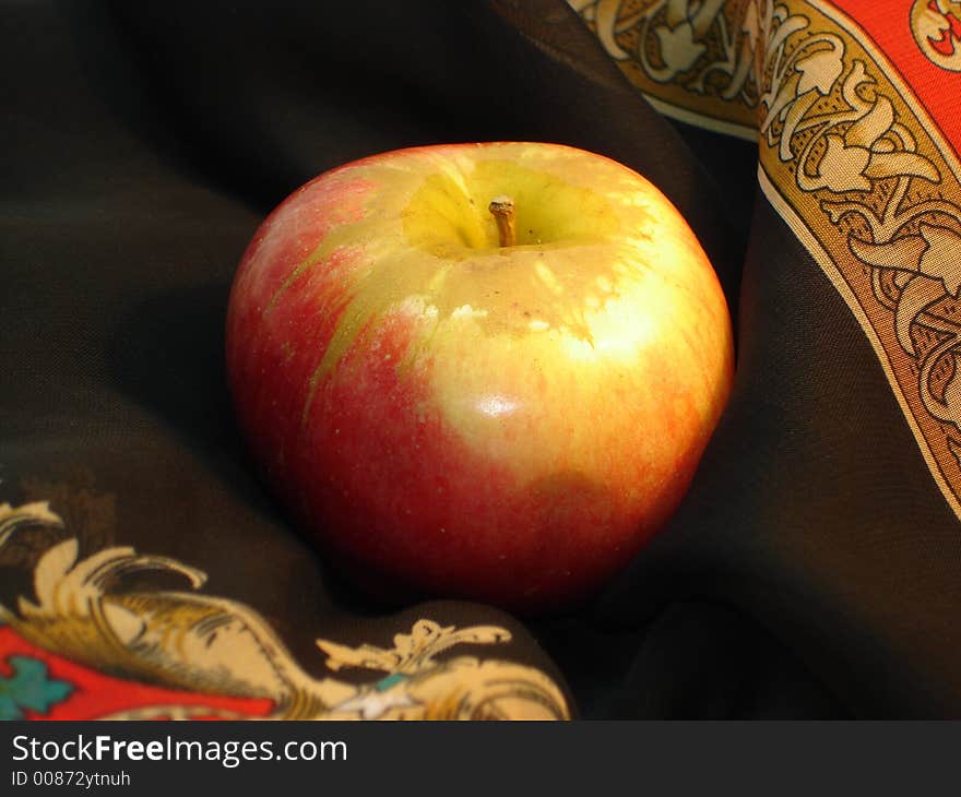 Delicious apple pretty. Yellow-red apple on a background of a black scarf with a yellow-red  ornament. Delicious apple pretty. Yellow-red apple on a background of a black scarf with a yellow-red  ornament