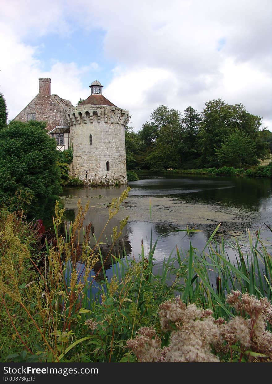 English country stone castle with round tower viewed from across moat with reflections of sky and clouds. English country stone castle with round tower viewed from across moat with reflections of sky and clouds