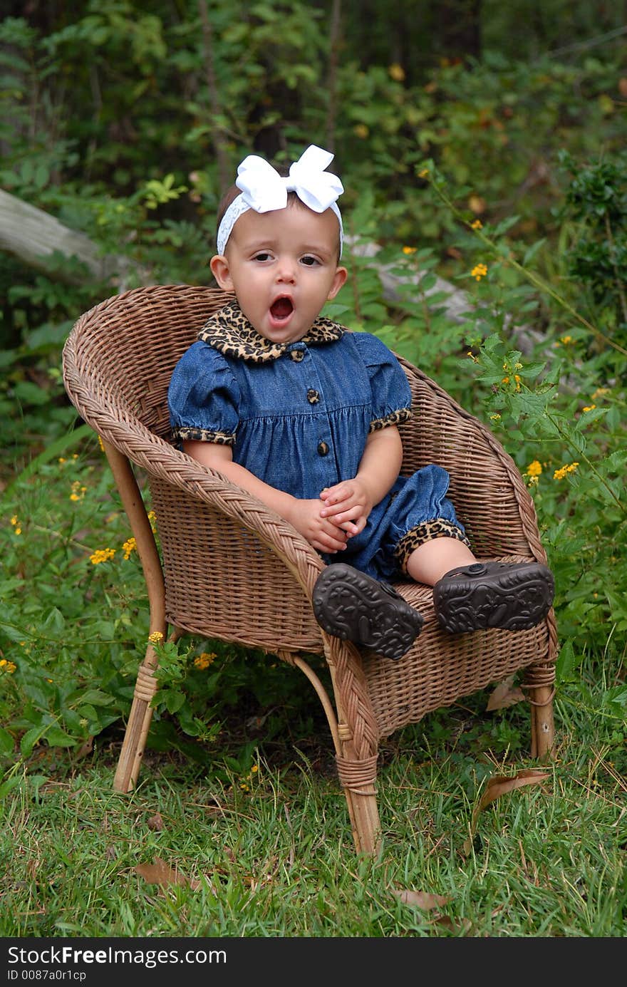 A darling baby girl sitting in a wicker chair wearing denim trimmed in leopard with a big bow in her hair outdoors. She's yawning so big - she must be really sleepy. A darling baby girl sitting in a wicker chair wearing denim trimmed in leopard with a big bow in her hair outdoors. She's yawning so big - she must be really sleepy