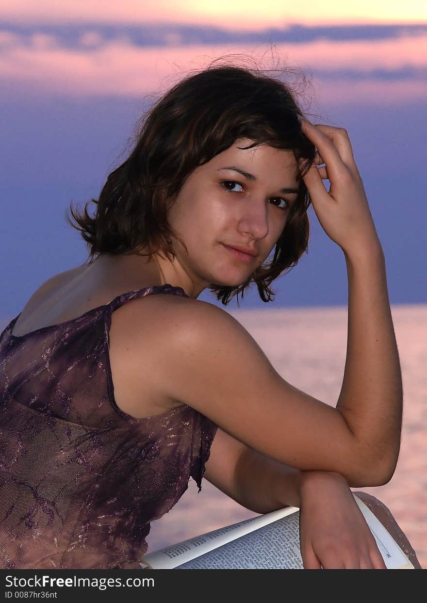 Young woman sitting at sunset, looking at camera  and smiling. Young woman sitting at sunset, looking at camera  and smiling