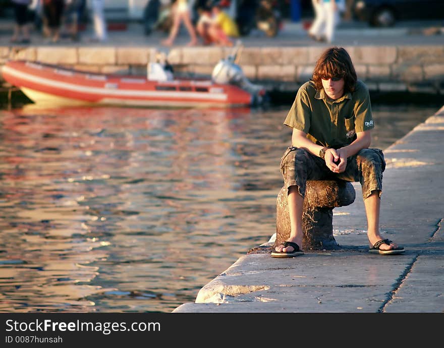 Teen boy sitting at the dock looking down, wide angle. Teen boy sitting at the dock looking down, wide angle