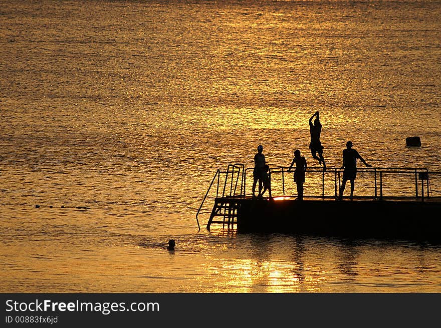 Silhouettes of people on a pier on a background of the orange sea. Silhouettes of people on a pier on a background of the orange sea