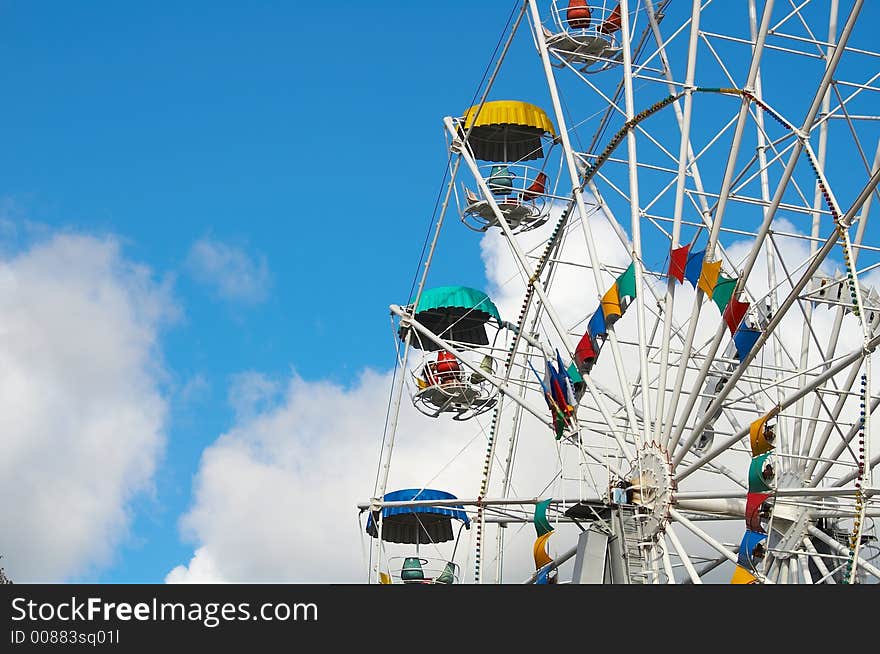 Part of a multi-coloured Ferris wheel on a background of the sky and clouds