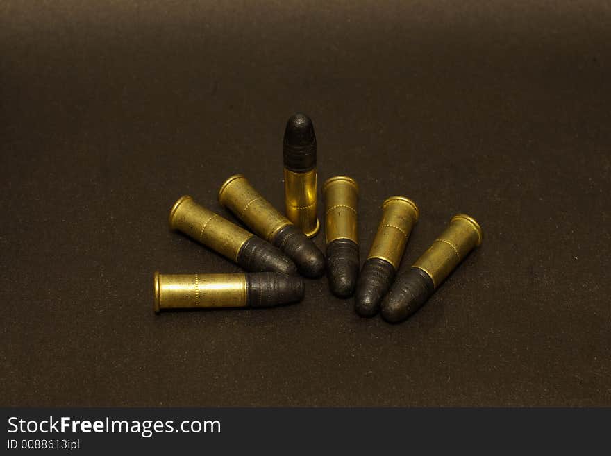 Seven .22lr cartridges in brass shells on black surface. Seven .22lr cartridges in brass shells on black surface