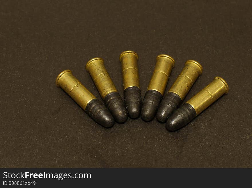 Six .22lr rimfire cartridges on black surface. Six .22lr rimfire cartridges on black surface