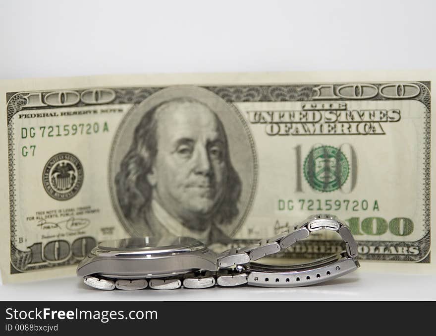 A wrist watch with the $100 bill in the background. Shallow depth of field, focus is on the watch. Time is money.