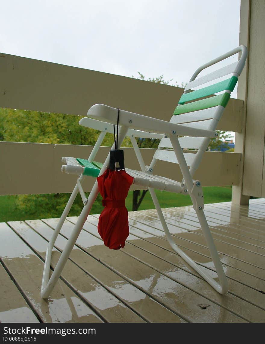 A picture of  an umbrella hanging on a rained soaked chair on a rain soaked porch. The person sitting there has gone inside. A picture of  an umbrella hanging on a rained soaked chair on a rain soaked porch. The person sitting there has gone inside.