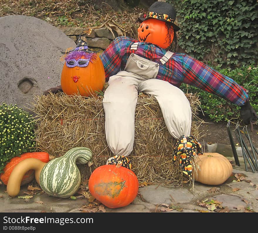 Halloween display with scarecrow, pumpkins, hay and mums.