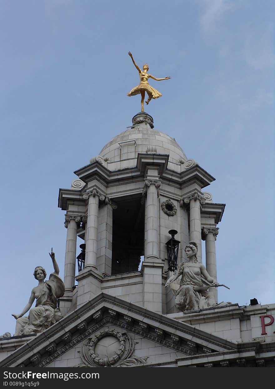 Gilded balerina sculpture on grey stone dome with columns and statues on building in London. Gilded balerina sculpture on grey stone dome with columns and statues on building in London