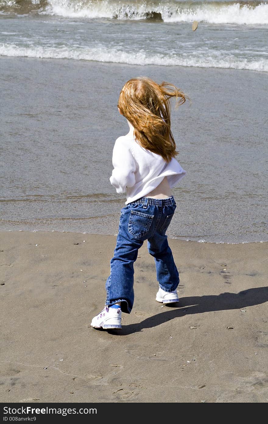 Small red read girl throws rocks into the lake on a windy day. Small red read girl throws rocks into the lake on a windy day.