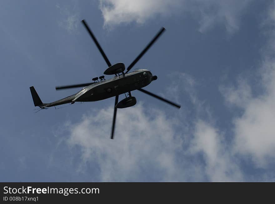 Military helicopter against blue sky with few clouds.