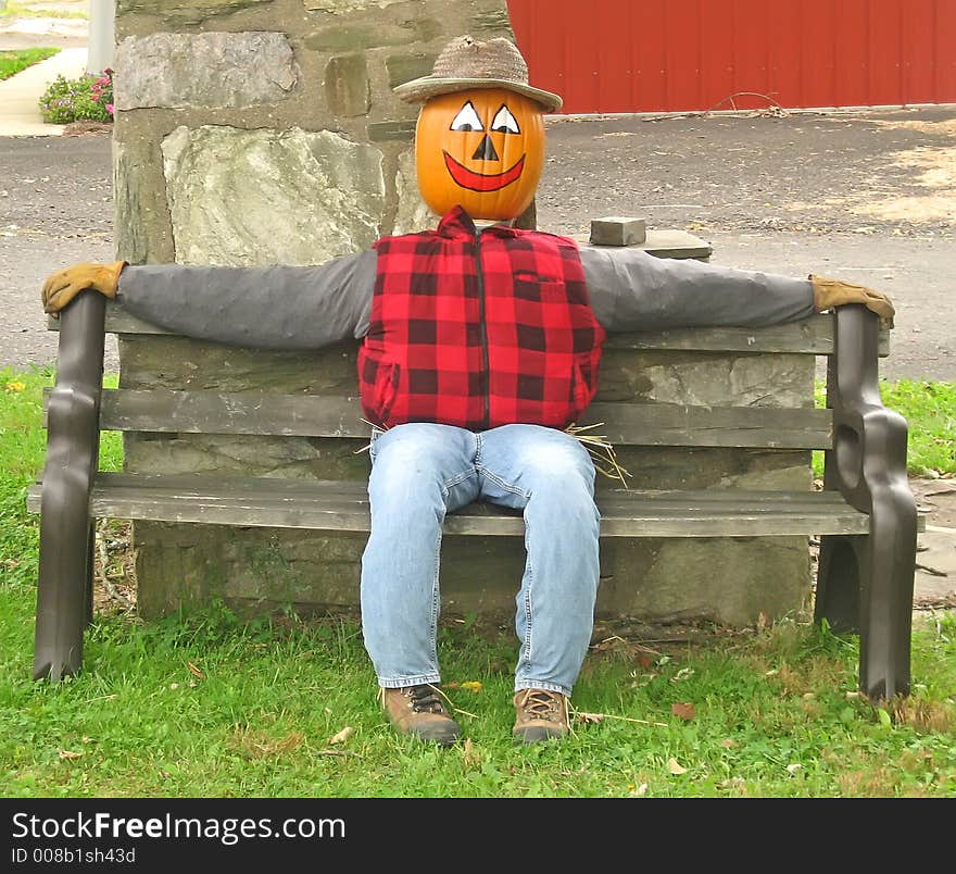 Pumpkin head scarecrow sitting on a bench. Pumpkin head scarecrow sitting on a bench.