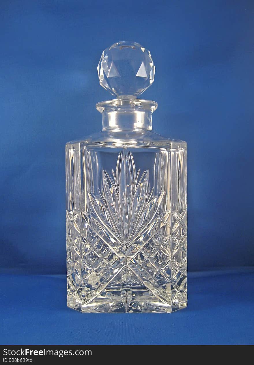 Empty crystal liquor decanter against a blue background. Empty crystal liquor decanter against a blue background.