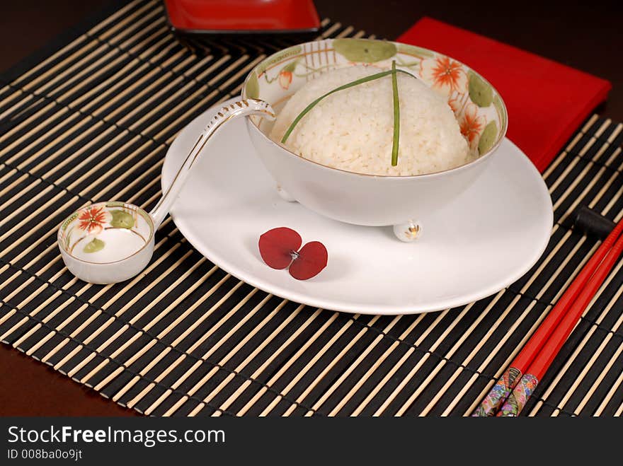 Bowl of rice with chives in antique Asian bowl with chopsticks on a bamboo placemat