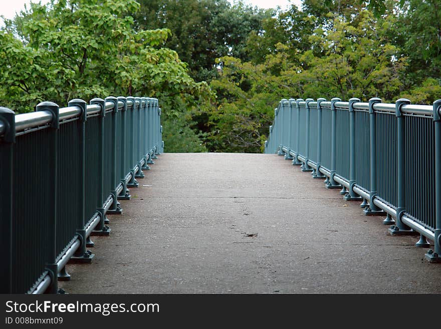 A walking bridge that crosses the charles river in watertown massachusetts, leading the viewer to a lush forest in the distance. A walking bridge that crosses the charles river in watertown massachusetts, leading the viewer to a lush forest in the distance