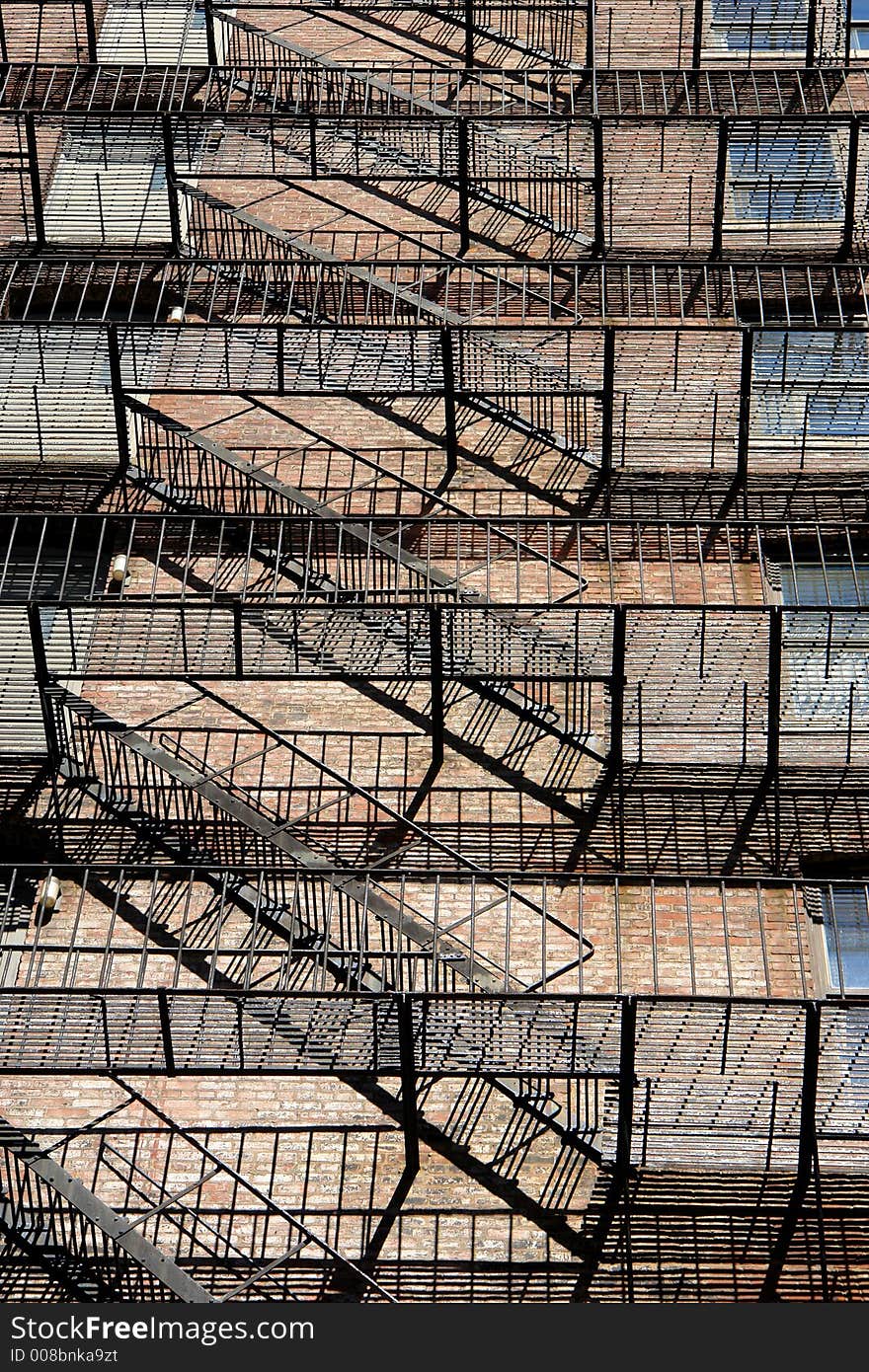 Zig zagging fire escape on back of old apartment building showing many floors and apartment windows