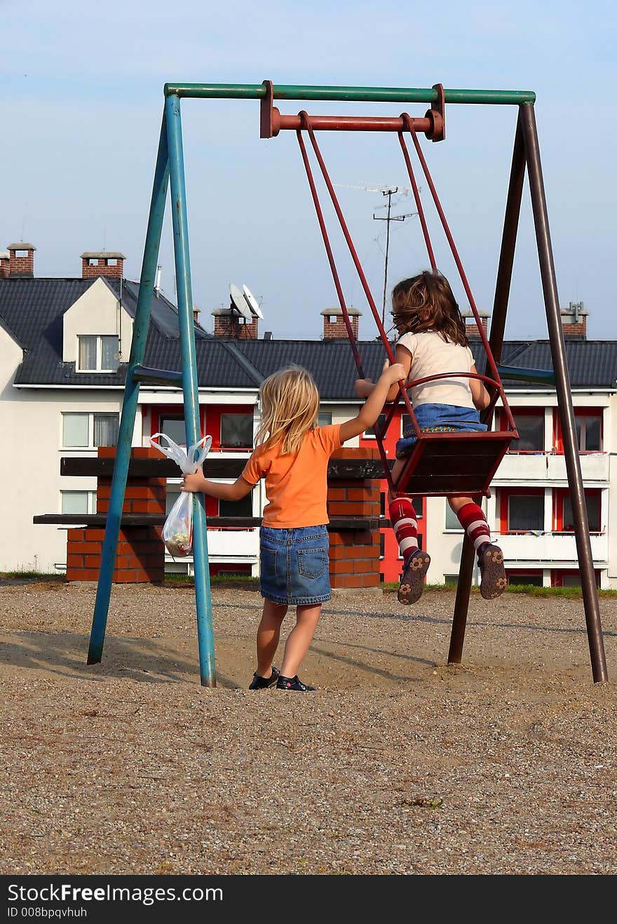 Swinging time; 
girl rocked girl on the swing; 
background city houses and sky