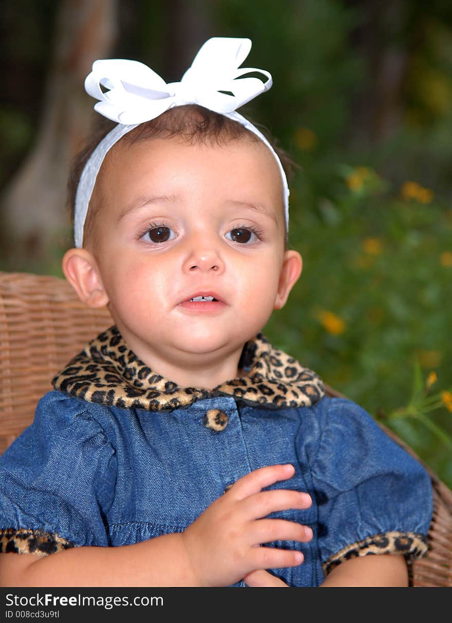 A cute little girl with a big bow in her hair sitting in a child's wicker chair wearing a denim outfit trimmed in leopard print. A cute little girl with a big bow in her hair sitting in a child's wicker chair wearing a denim outfit trimmed in leopard print