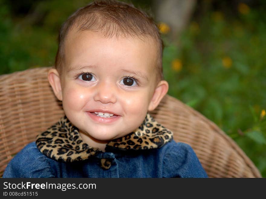 A cute little girl sitting in a child's wicker chair wearing a denim outfit trimmed in leopard print. A cute little girl sitting in a child's wicker chair wearing a denim outfit trimmed in leopard print