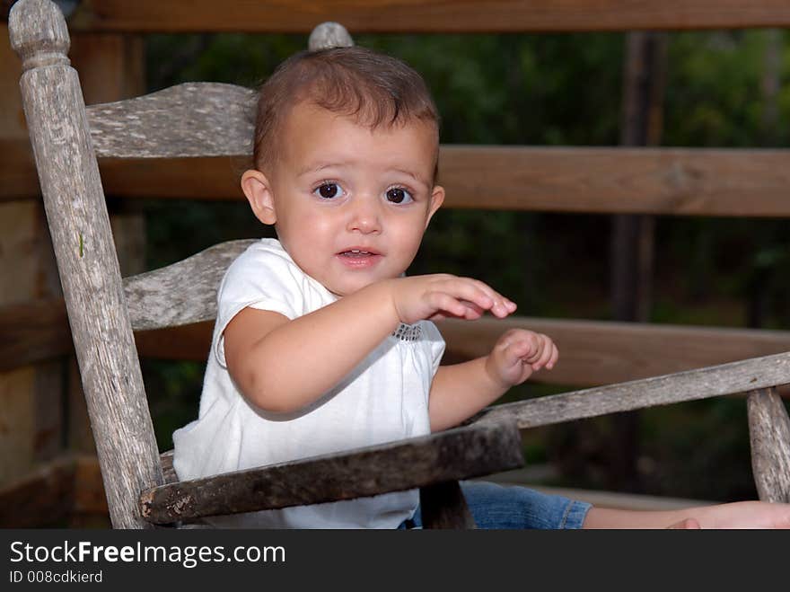 A beautiful little girl with big brown eyes and a sweet expression rocking in an old rocker. A beautiful little girl with big brown eyes and a sweet expression rocking in an old rocker