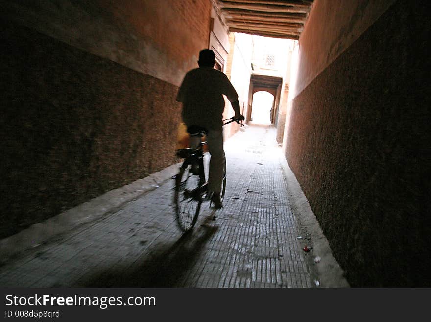A man rides his bicycle on an empty narrow street. A man rides his bicycle on an empty narrow street