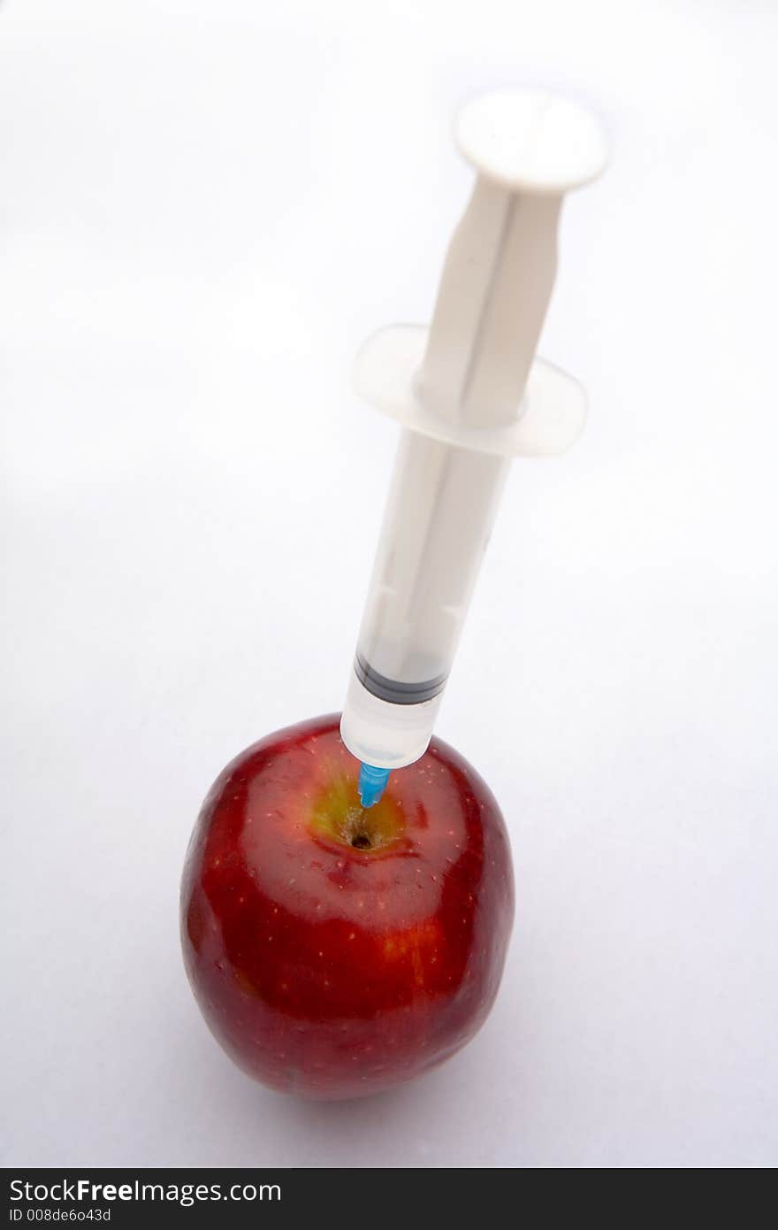 A bright red apple being injected with a clear syringe. Illustrating food safety issues, Genetic engineering, and health. A bright red apple being injected with a clear syringe. Illustrating food safety issues, Genetic engineering, and health.