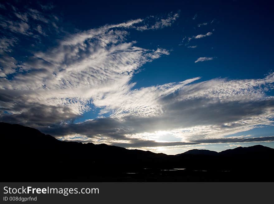 Clouds backlit by a setting sun with a mountain range in the foreground. Clouds backlit by a setting sun with a mountain range in the foreground.