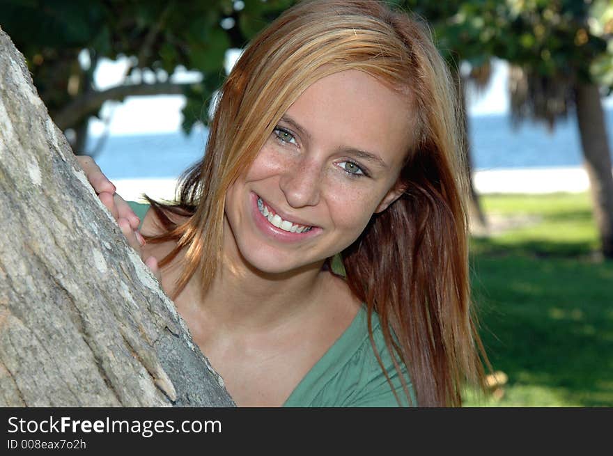 A pretty teenager peaking out from a  tree in the park. A pretty teenager peaking out from a  tree in the park