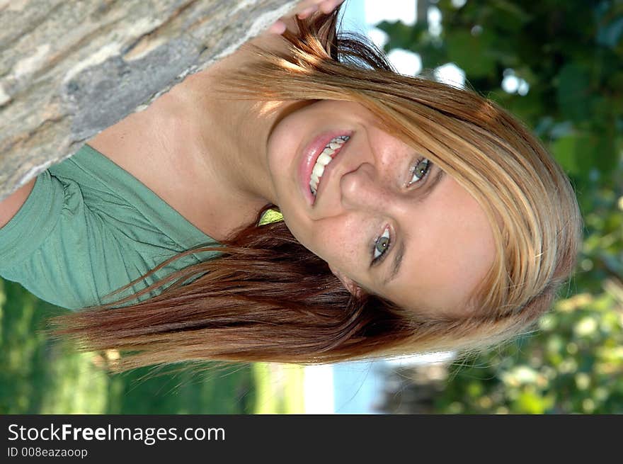 A pretty teenager peaking out from a tree in the park. A pretty teenager peaking out from a tree in the park