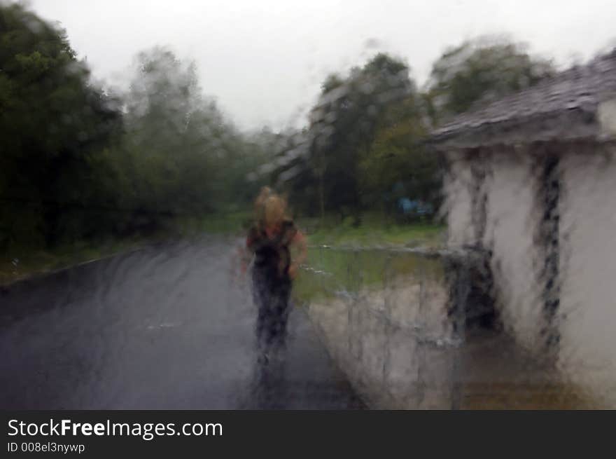 A young woman walking through the pouring rain. (Taken through a rain drenched glass window and therefore a blurred picture enhancing the visual effect of the downpour). A young woman walking through the pouring rain. (Taken through a rain drenched glass window and therefore a blurred picture enhancing the visual effect of the downpour).