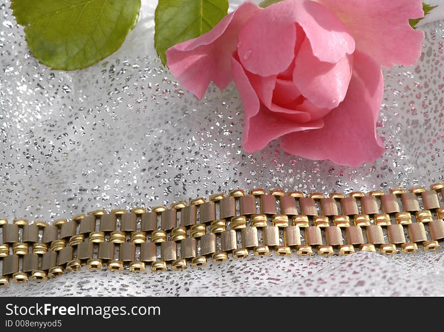 A gold bracelet with a pink rose