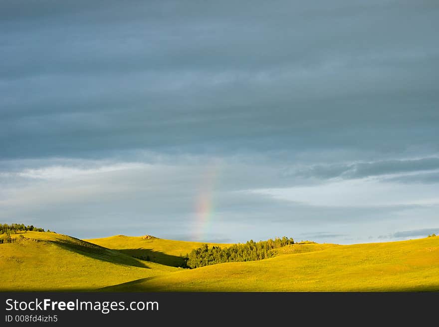 Cloudy sky with rainbow and fields