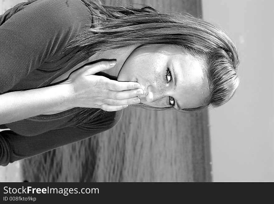 A pretty teenager with her hands over her mouth indicating silence in black and white