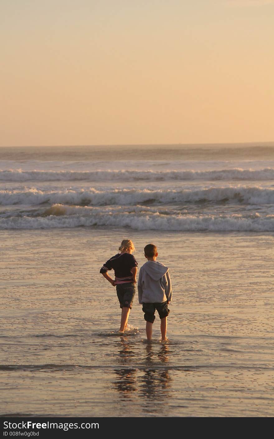 Two children waiting for the next wave to come in..lit by the late evening sun. Two children waiting for the next wave to come in..lit by the late evening sun.