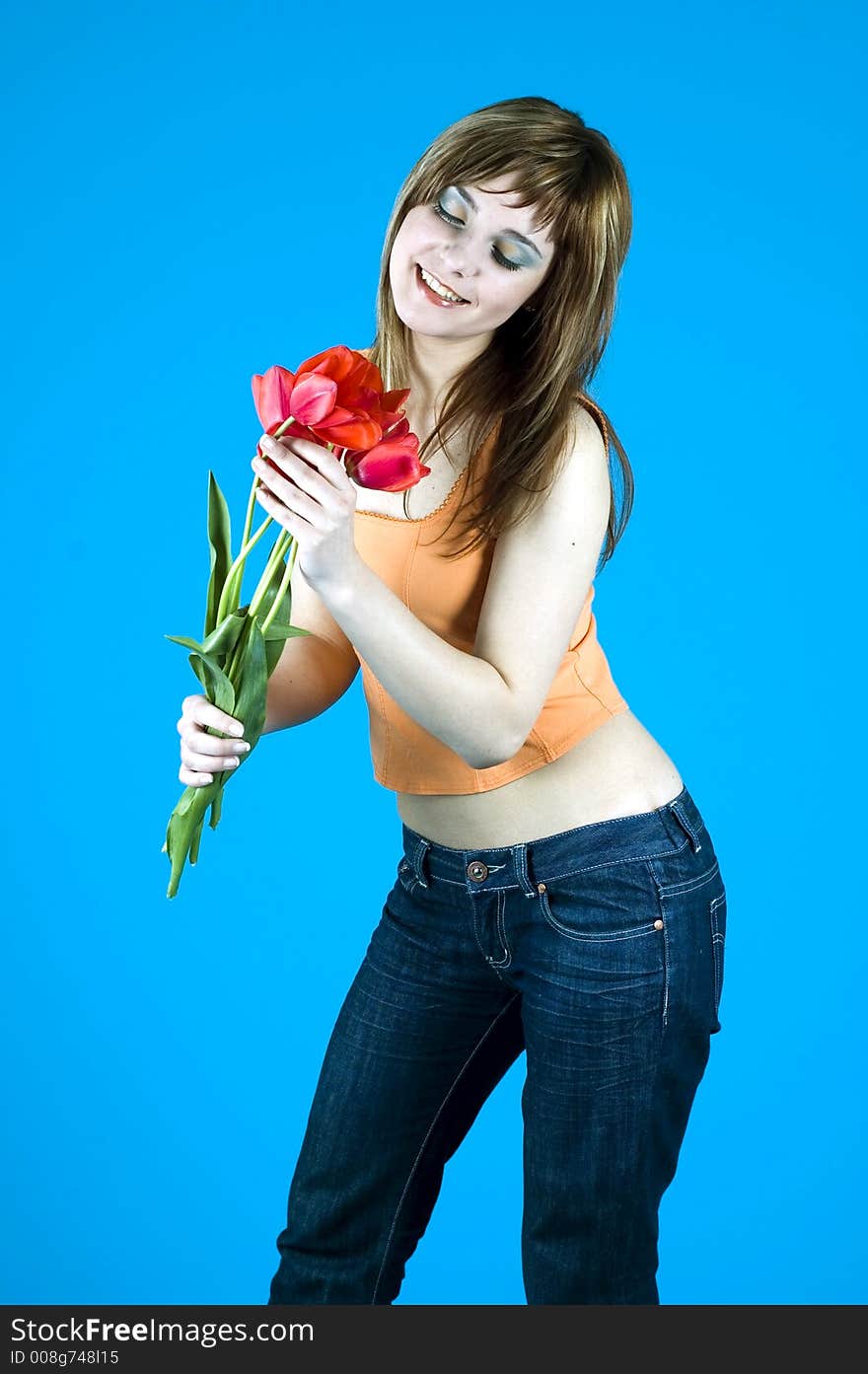 Portrait of a young girl smiling and looking at a bouquet of tulips, expression of youth and happiness; nice make-up, isolated on blue background. Portrait of a young girl smiling and looking at a bouquet of tulips, expression of youth and happiness; nice make-up, isolated on blue background