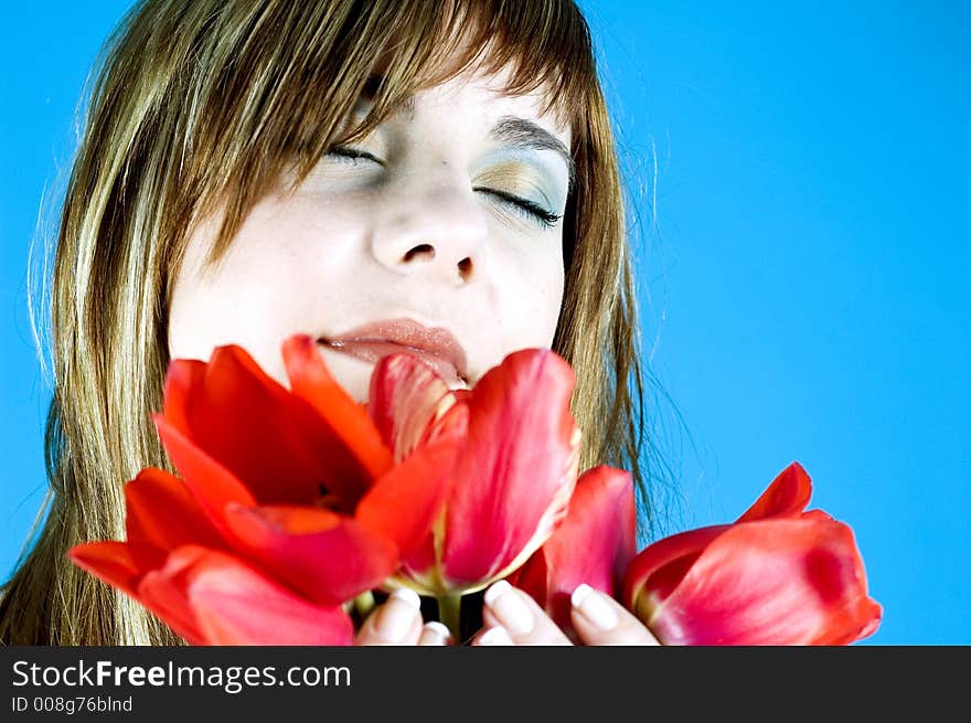 Portrait of a young beautiful girl, smelling a bouquet of tulips and looking relaxed due to the nice scent of the flowers; expression of youth and senses; isolated on blue. Portrait of a young beautiful girl, smelling a bouquet of tulips and looking relaxed due to the nice scent of the flowers; expression of youth and senses; isolated on blue.