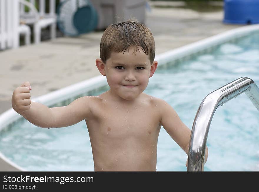 Young boy flexing muscle poolside. Young boy flexing muscle poolside