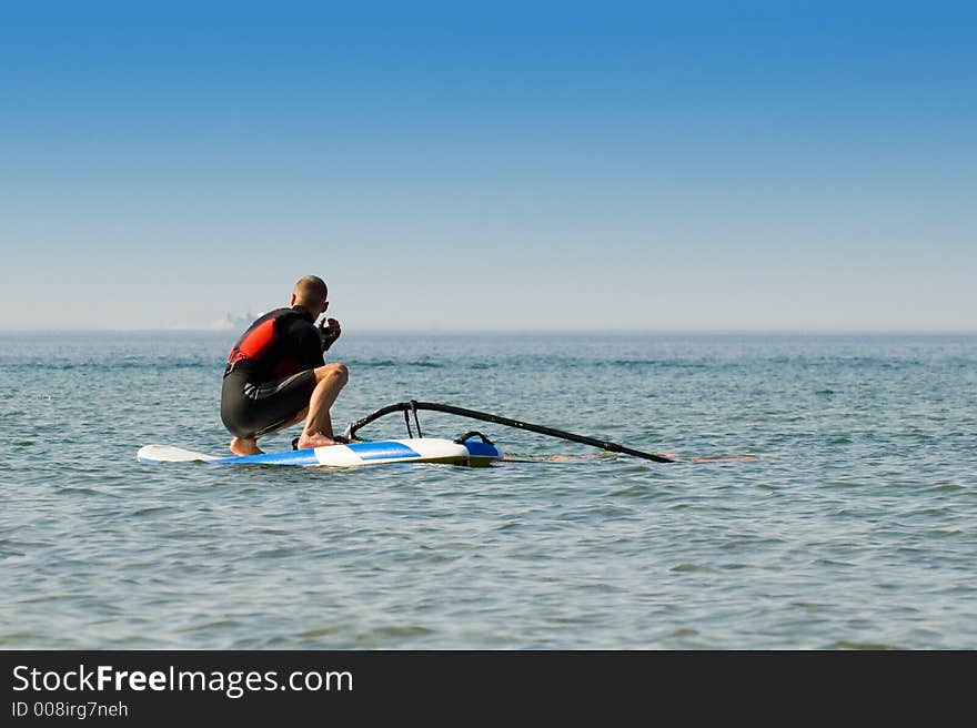 Windsurfer waiting for the wind at sea on a sunny day. Windsurfer waiting for the wind at sea on a sunny day.