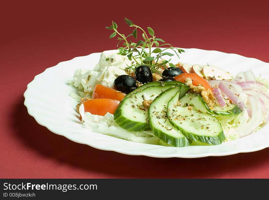 Healthy feta-cheese salad with fresh cucumber, tomatoes, apple and onion slices and olives over royal red background
