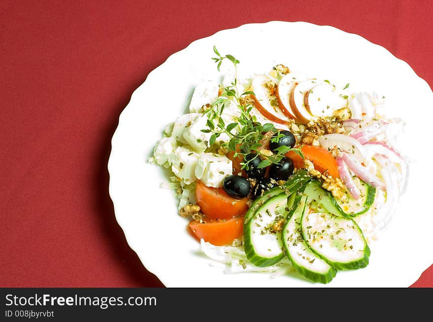 Healthy feta-cheese salad with fresh cucumber tomato apple and onion slices and olives over royal red background