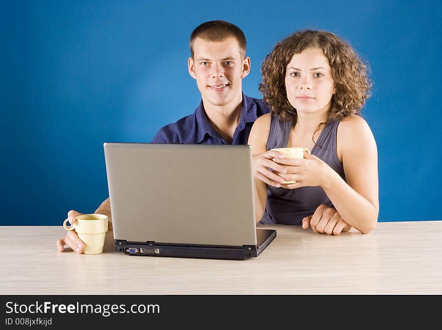 Young couple at the table with laptop + blue background