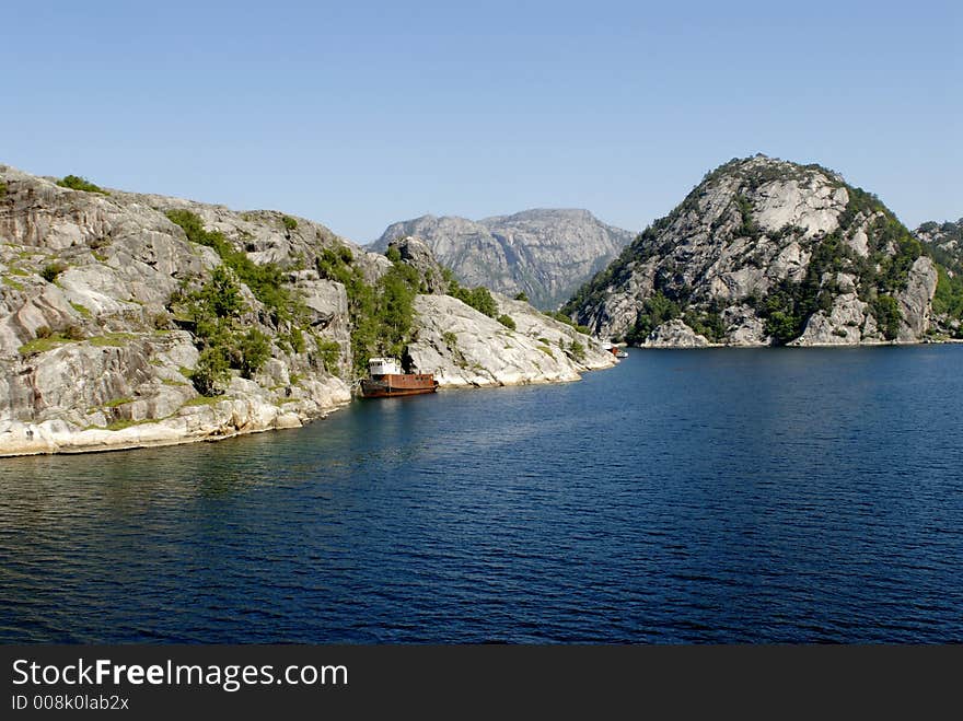 Picture of shipwreck in fjord near rocky coast.