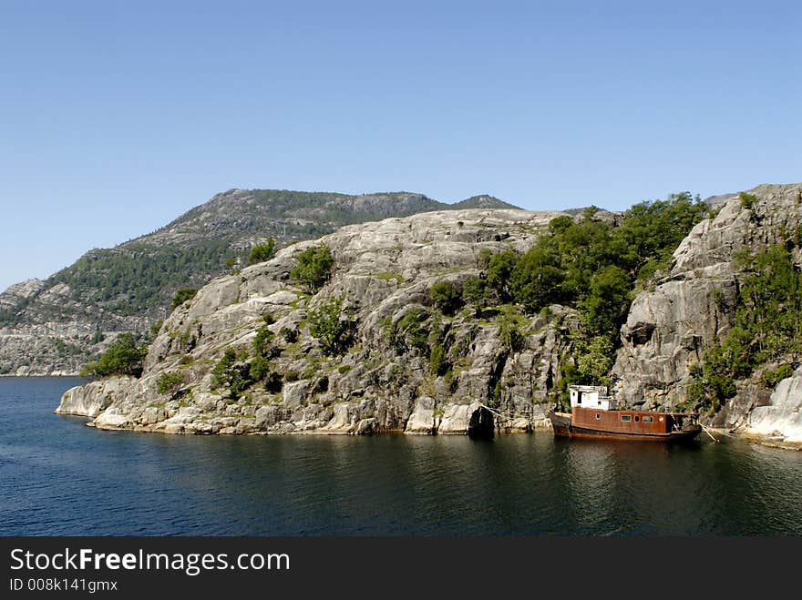 Picture of shipwreck in fjord near rocky coast.