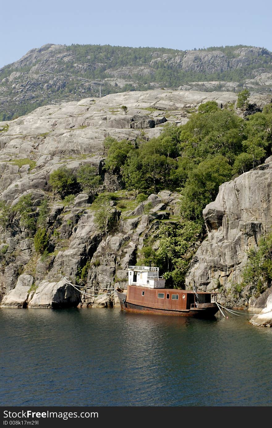 Picture of shipwreck in fjord near rocky coast.